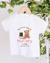 A white t-shirt with a teddy bear and a chalkboard, along with the text "My First Day at Nursery Lisa" and "September 2020".