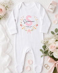 A white onesie with a pink floral design and the text "Siena Flower Girl" is displayed on a white background, accompanied by a pink ribbon, a ring box, and a bouquet of white flowers.
