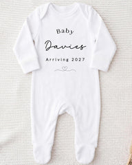 A white onesie with the text "Baby Davies Arriving 2027" printed on it.