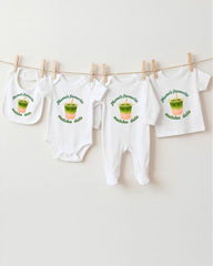 A collection of four white baby clothes, including onesies and bibs, hanging on a clothesline.