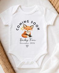 A white baby onesie with a graphic of a fox and the text "Coming soon Baby Fox December 2026" printed on it.