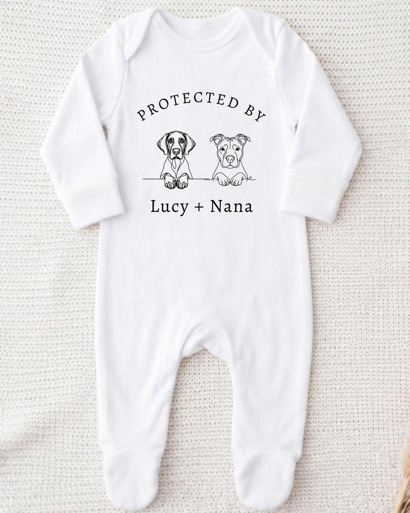 A white bodysuit with a graphic design featuring two cartoon dogs and the text "PROTECTED BY Lucy + Nana" printed on it.