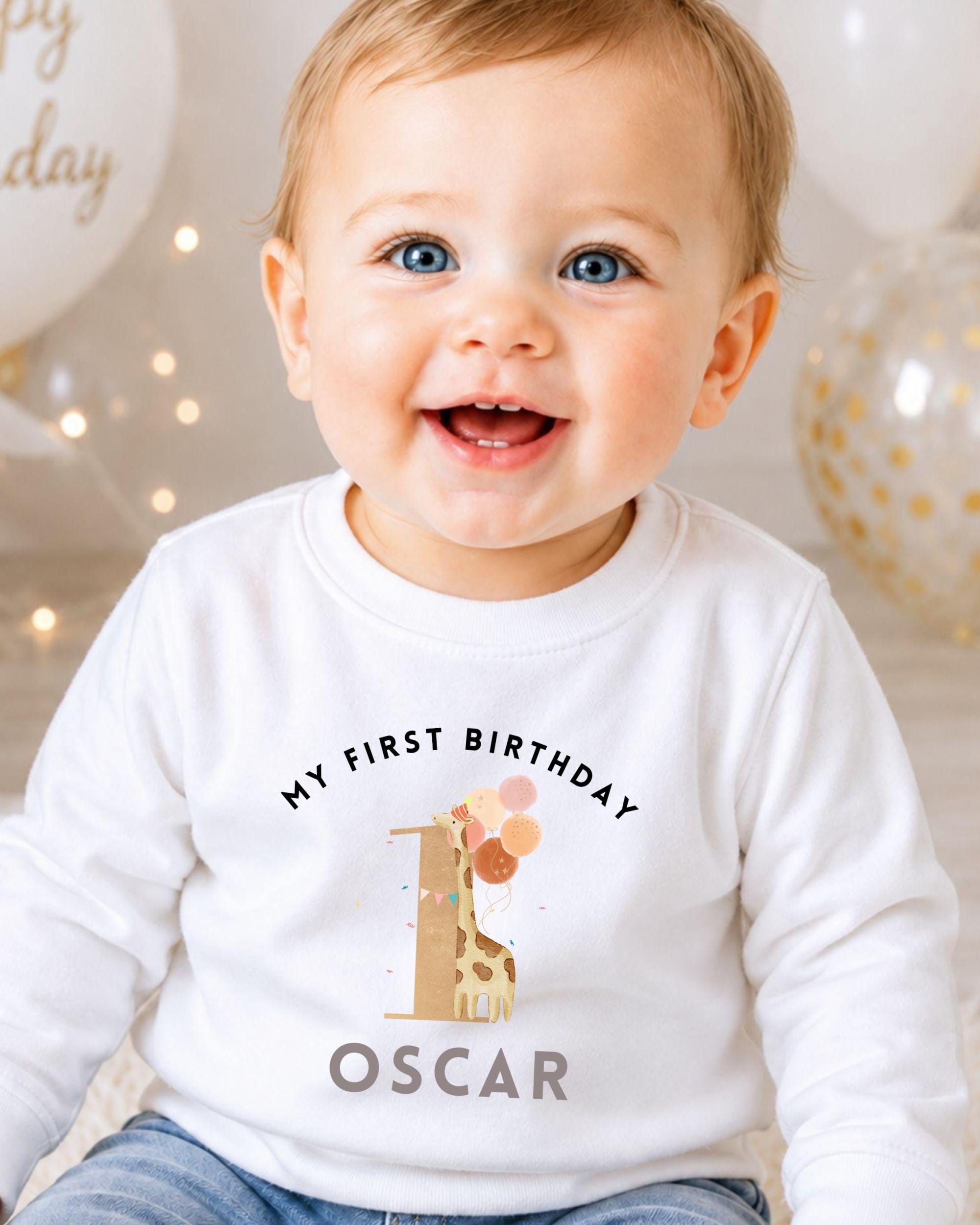 A smiling baby boy wearing a white shirt with a giraffe and the text "My first birthday Oscar" printed on it.