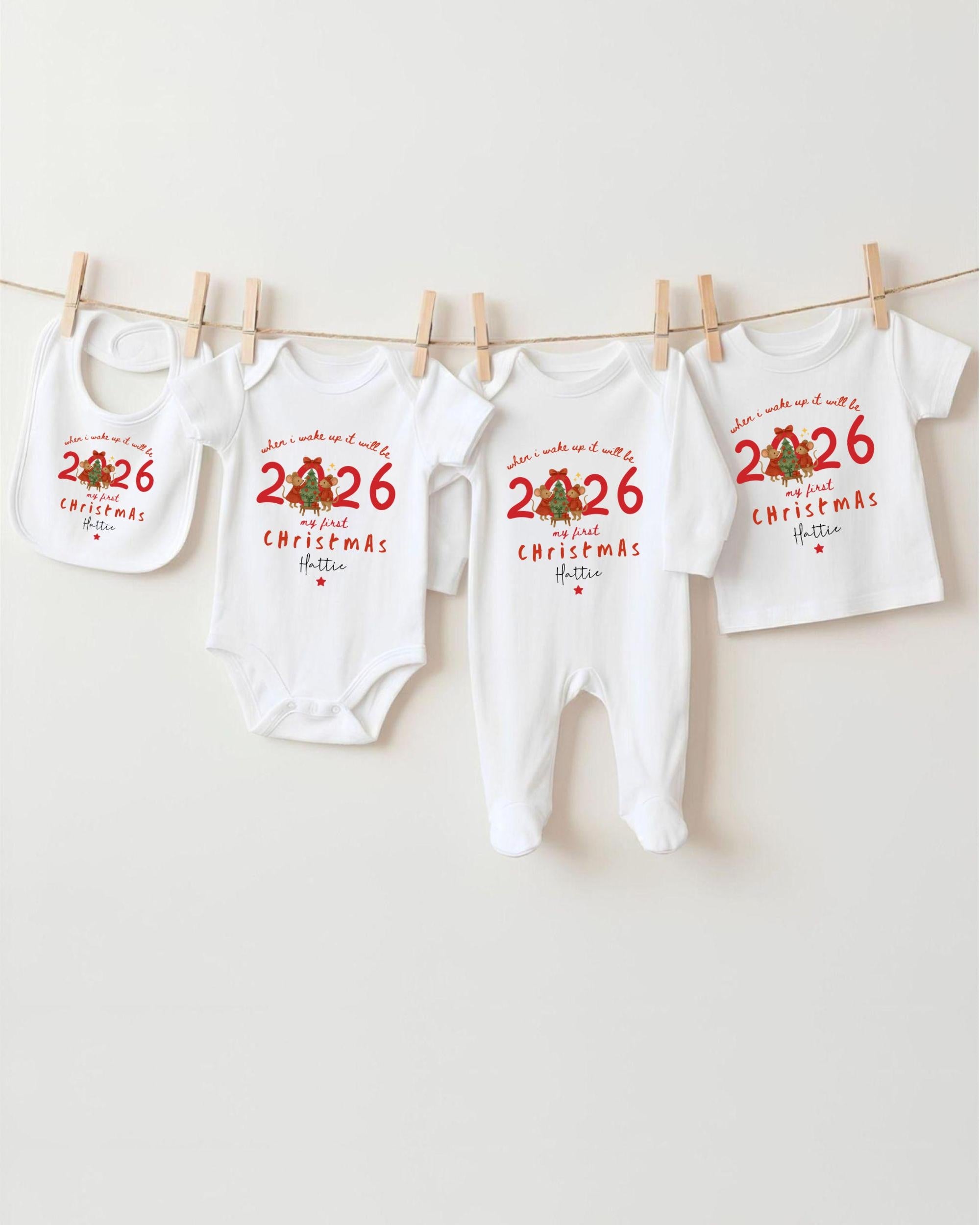 A row of white Christmas-themed baby clothes, including onesies and bibs, hanging on a clothesline.