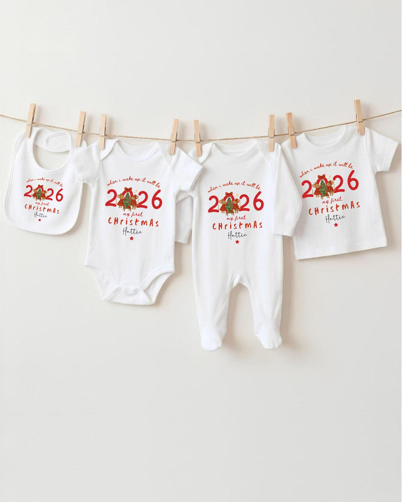 A row of white Christmas-themed baby clothes, including bodysuits and bibs, hanging on a clothesline.