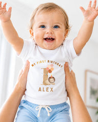 A smiling baby wearing a white t-shirt with a personalized birthday message and a cartoon character.
