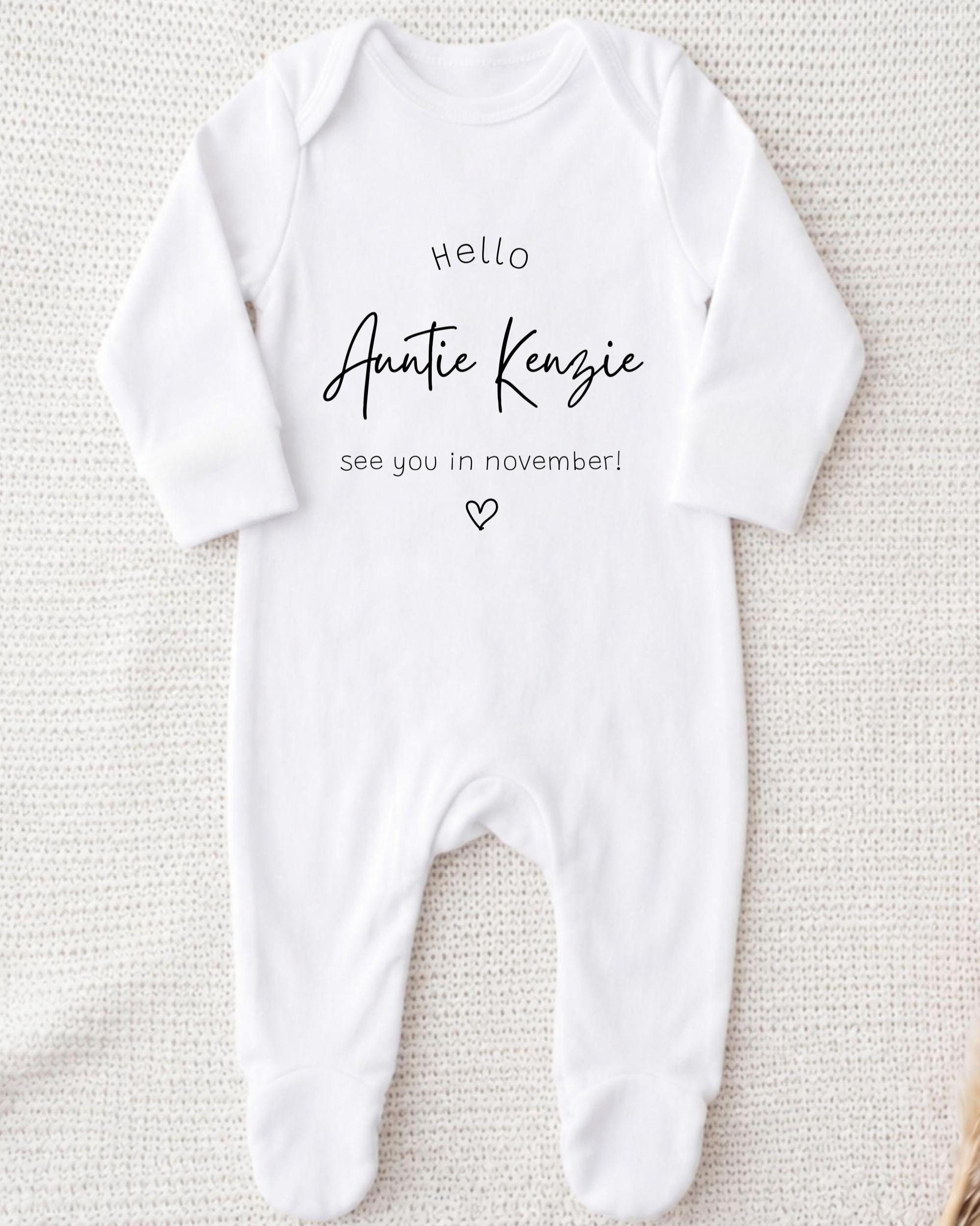 A white onesie with the text "Hello Auntie Kenzie" printed on it, along with a heart symbol.