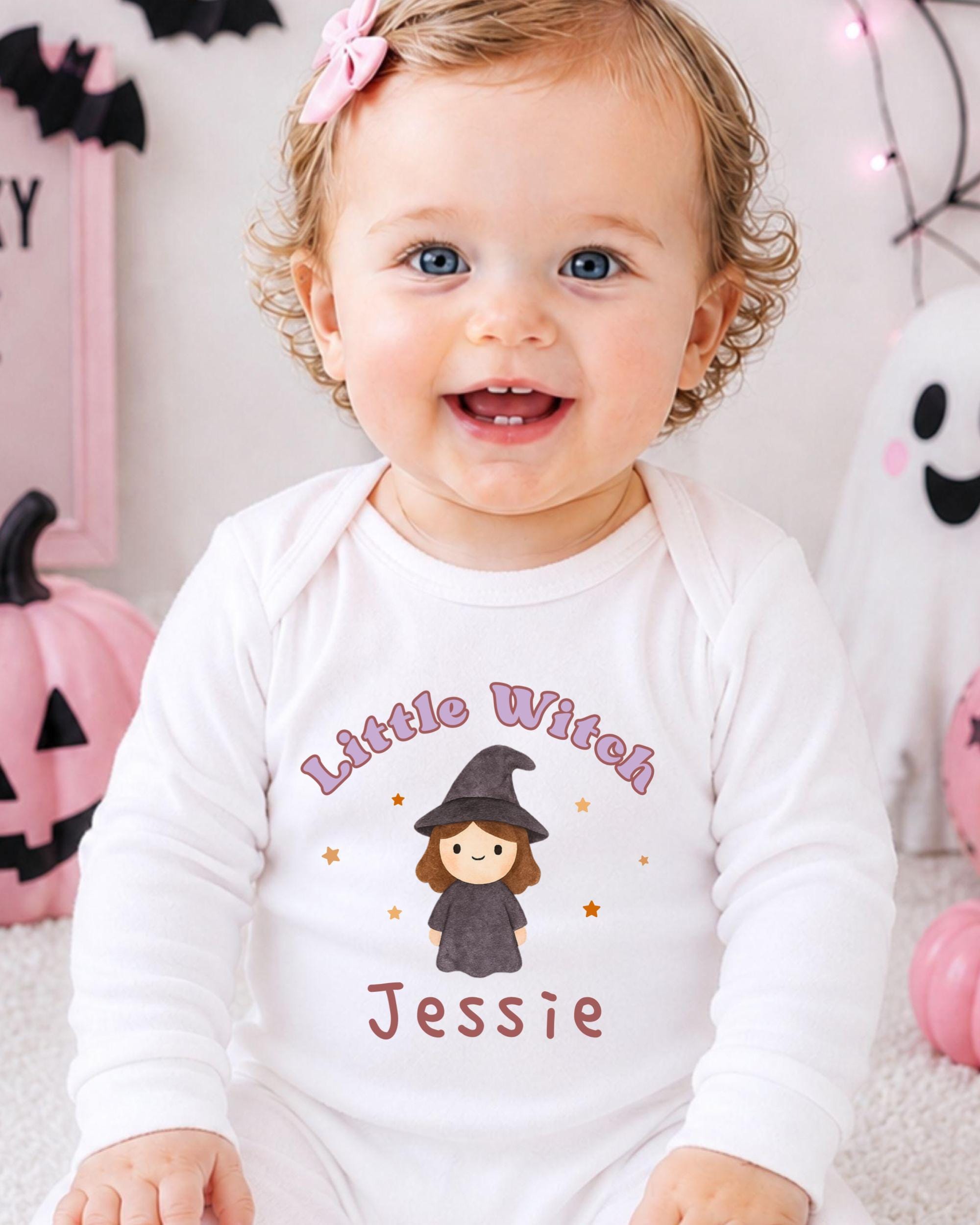 A smiling baby girl wearing a white onesie with a witch design and the name " Jessie" printed on it.