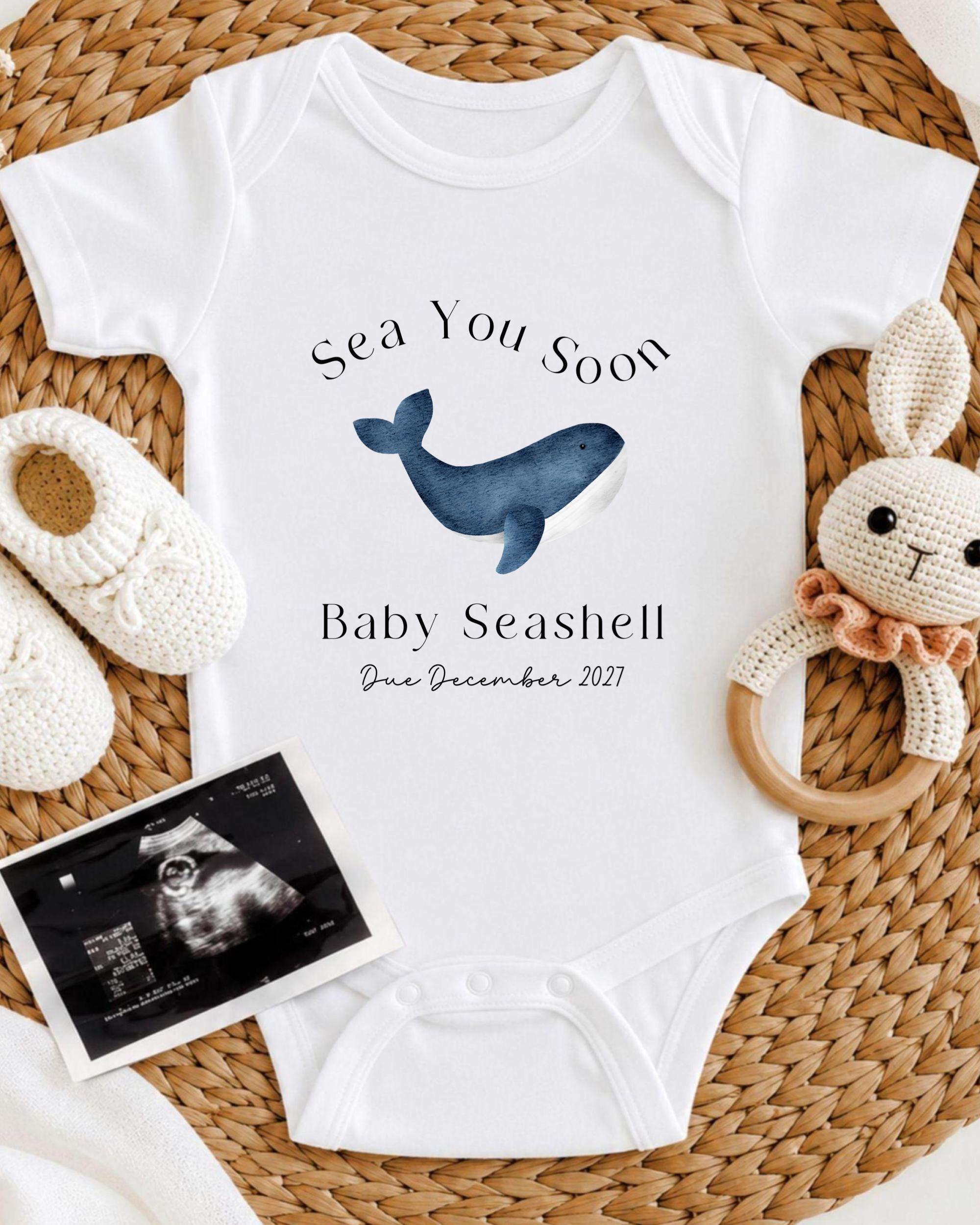 a baby announcement, including a white onesie with a blue whale graphic, a crocheted bunny toy, and a baby announcement photo.