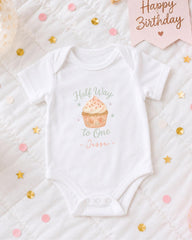 A white onesie with a cupcake design and the text "Half Way to One - Jesse" printed on it, along with confetti and a birthday card.