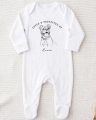 A white onesie with a black and white illustration of a dog and the text "LOVED & PROTECTED BY" printed on it.