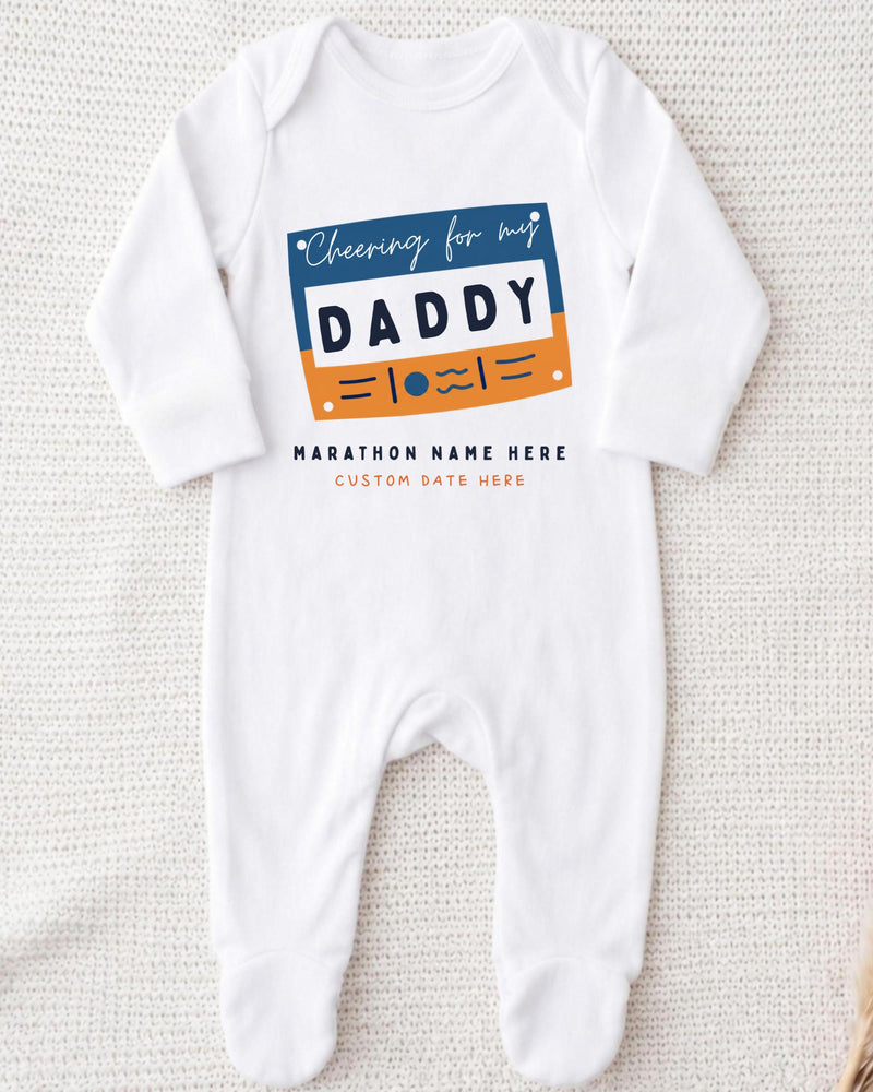 A white onesie with a graphic design on it, featuring the text "Cheering for my DADDY" and "MARCHON NAME HERE" along with a custom name.