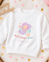 A white sweatshirt with a mermaid graphic and the text "Birthday Girl Jessica" printed on it, surrounded by confetti.