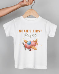 A white t-shirt with a pink airplane graphic and the text "Noah's first flight" printed on it.