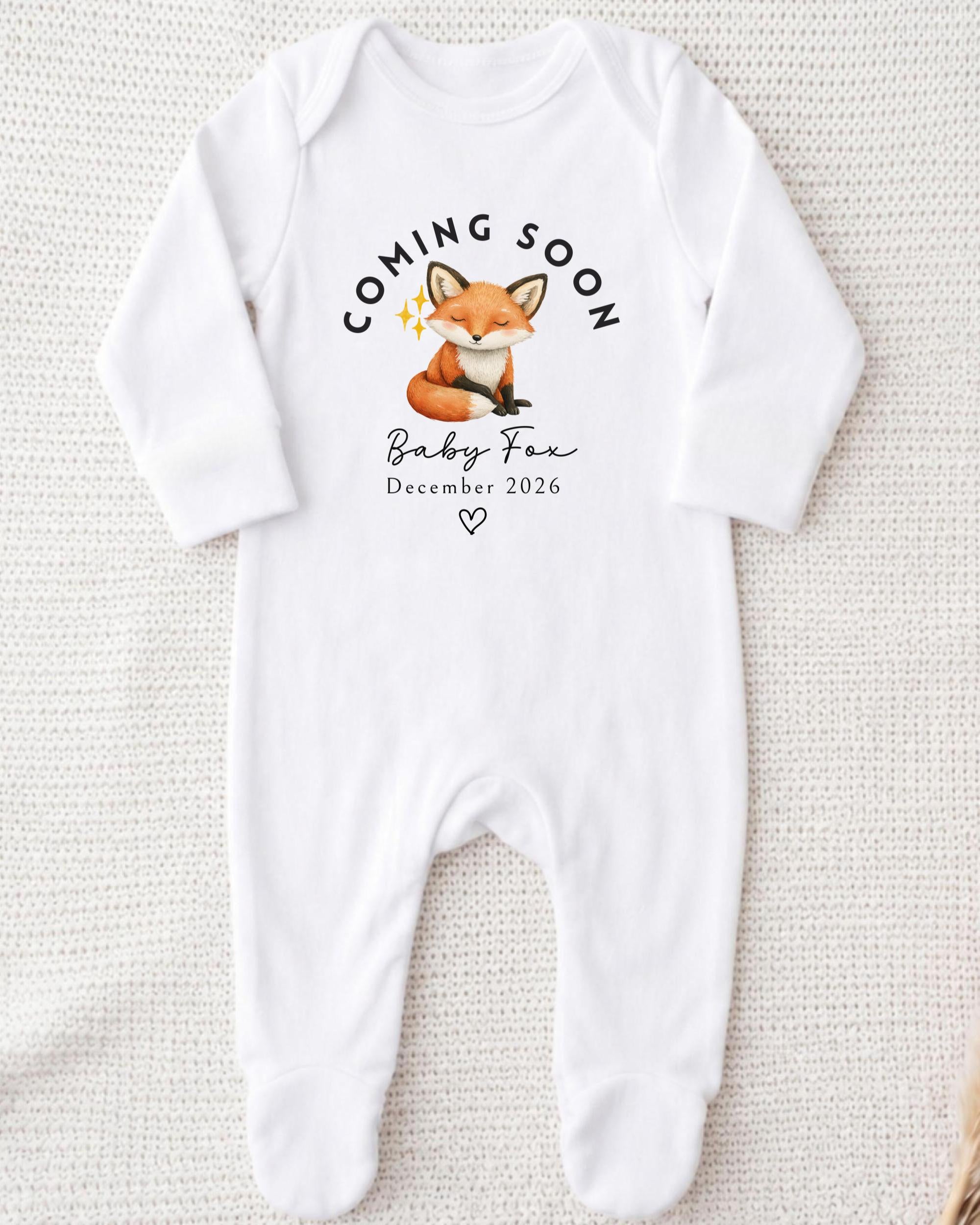 A white onesie with a graphic of a fox and text that announces the arrival of a baby fox.