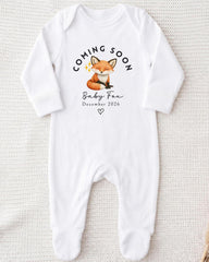 A white onesie with a graphic of a fox and text that announces the arrival of a baby fox.
