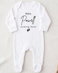 A white onesie with the text "Baby Powell Coming Soon" printed on it.