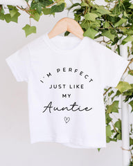 A white t-shirt with the text "I'M PERFECT JUST LIKE MY AUNTIE" printed on it, along with a heart symbol.
