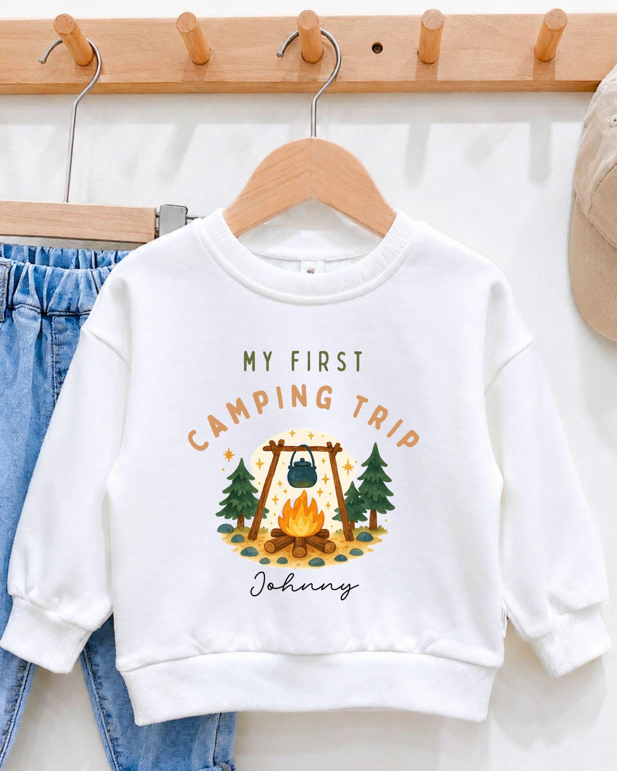 A white sweatshirt with a camping-themed design and text, hanging on a wooden hanger.