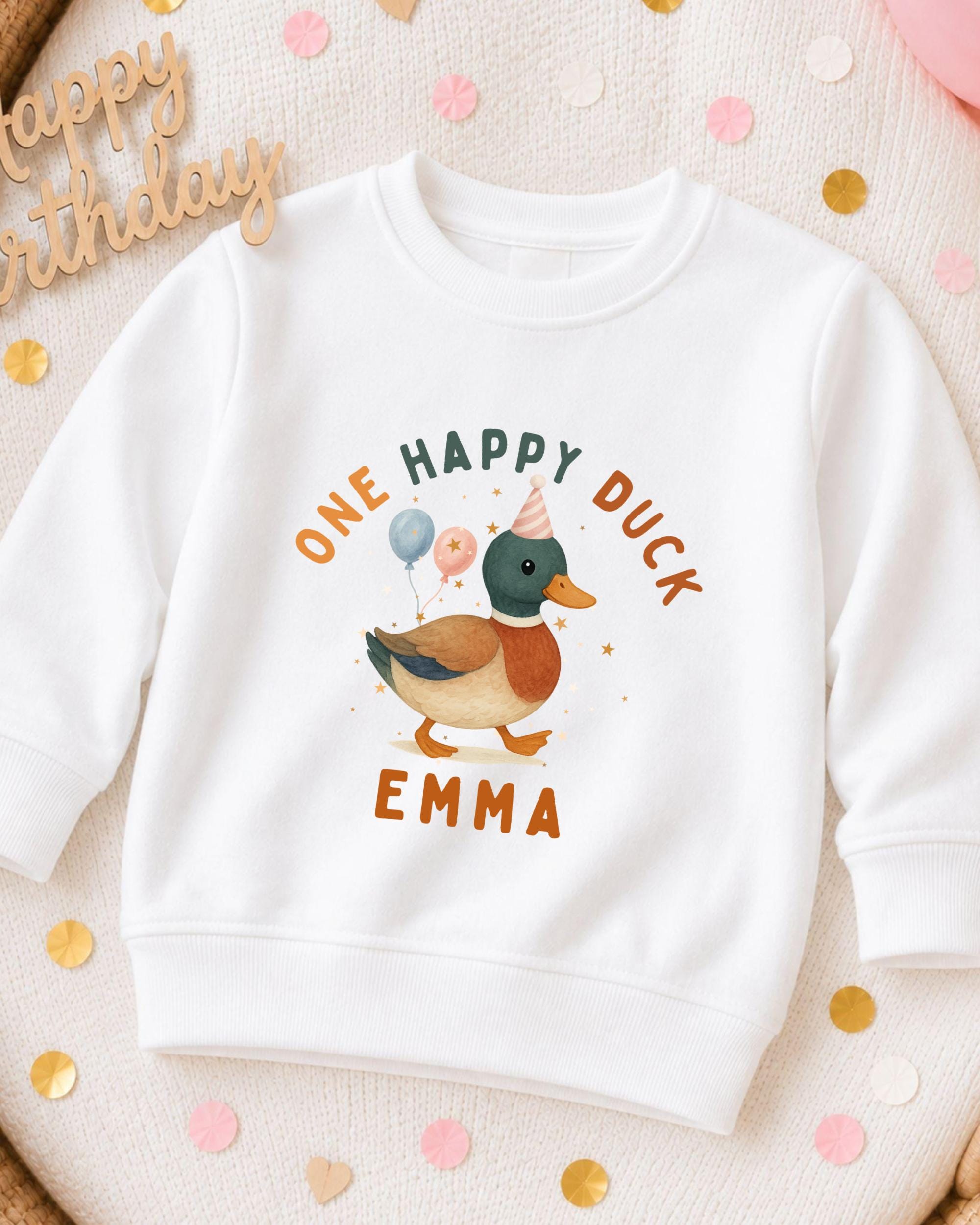 A white sweatshirt with a cartoon duck and the text "One Happy Duck Emma" printed on it, surrounded by confetti.