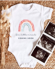 A white baby onesie with a rainbow graphic and the text "Our little miracle coming soon" is displayed alongside three black and white newborn images.