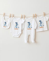 A collection of white baby clothes, including onesies and pants, with the name "James" printed on them. The clothes are hanging on a clothesline, with the first two items being bibs and the third one being a regular-sized shirt.
