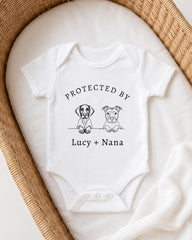 A white baby onesie with a graphic design of two dogs and the text "PROTECTED BY LUCY + NANA" printed on it.