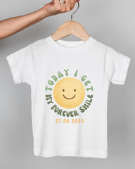 A white t-shirt with a yellow smiley face graphic and text printed on it.