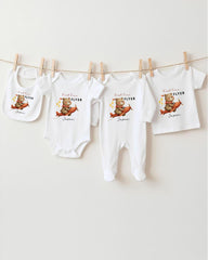 A row of four white baby clothes with a teddy bear design, hanging on a clothesline.