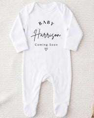 A white onesie with the text "BABY Harrison Coming Soon" printed on it.