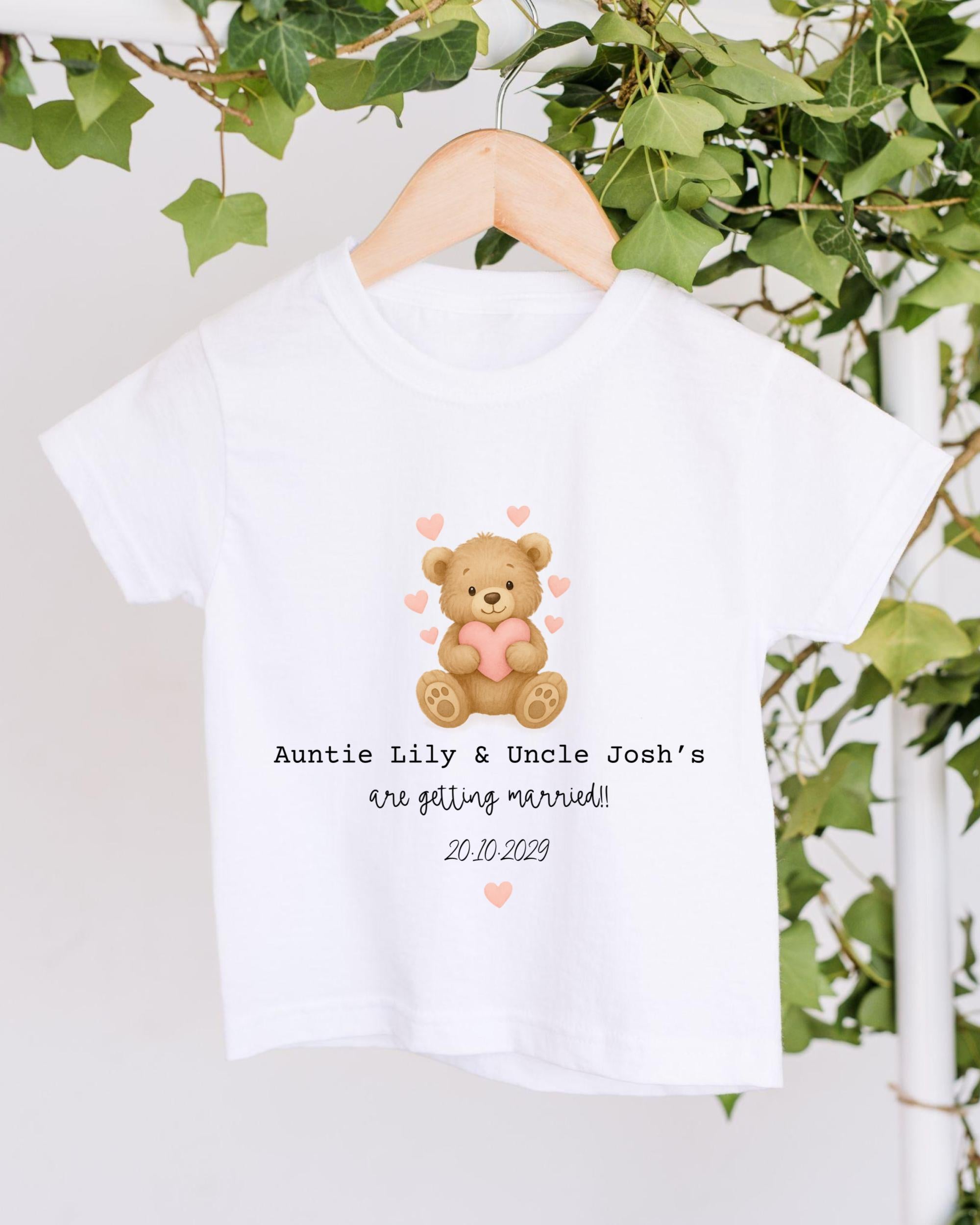 A white t-shirt with a graphic of a teddy bear holding a heart and the text "Auntie Lily & Uncle Josh's are getting married! 20.10.2029" printed on it.