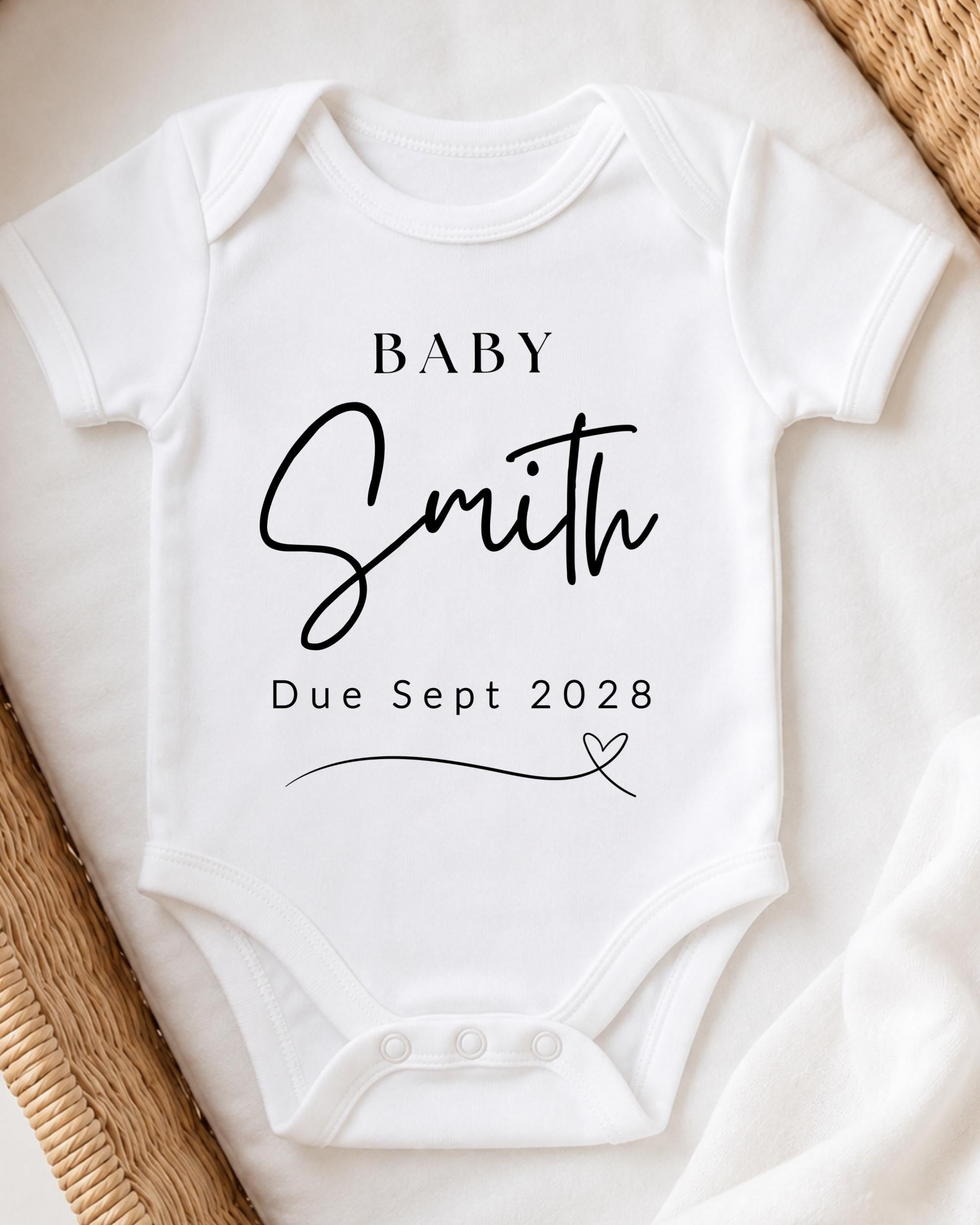 A white baby onesie with the text "BABY Smith Due Sept 2028" printed on it.