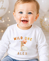A smiling baby boy wearing a white shirt with a graphic and text on it.