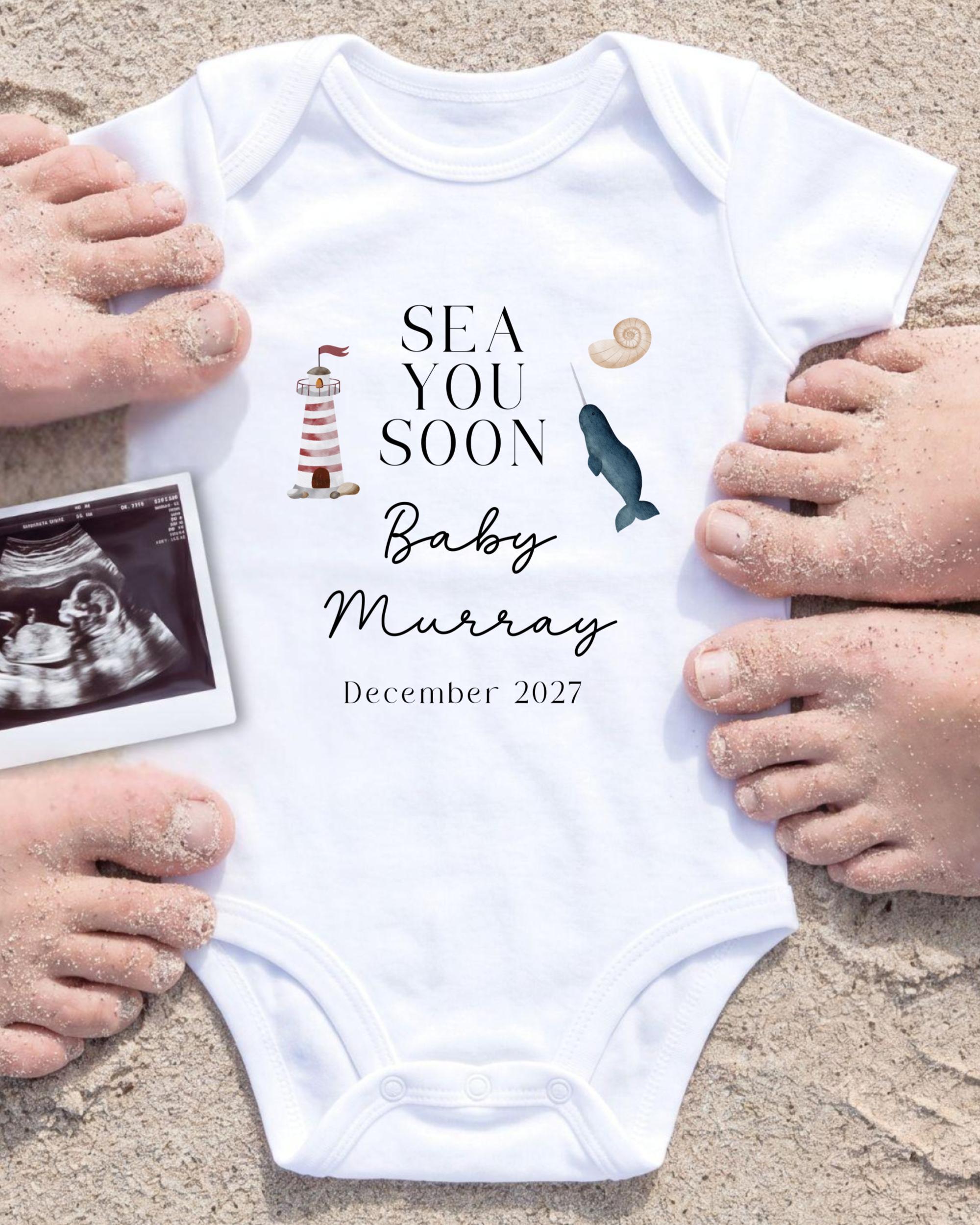 a white onesie with text and illustrations related to a baby announcement, surrounded by sand and a photograph of an Ultrasound image.