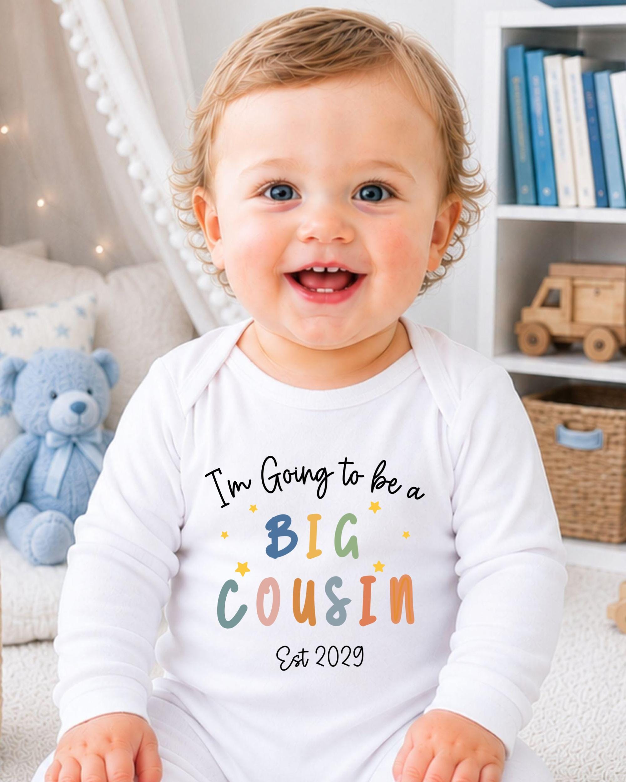 A smiling baby wearing a white onesie with text that says "I'm going to be a big Cousin Est 2029".