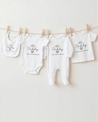 A row of four white baby clothes with the text "The Daddy" printed on them, hanging on a clothesline.