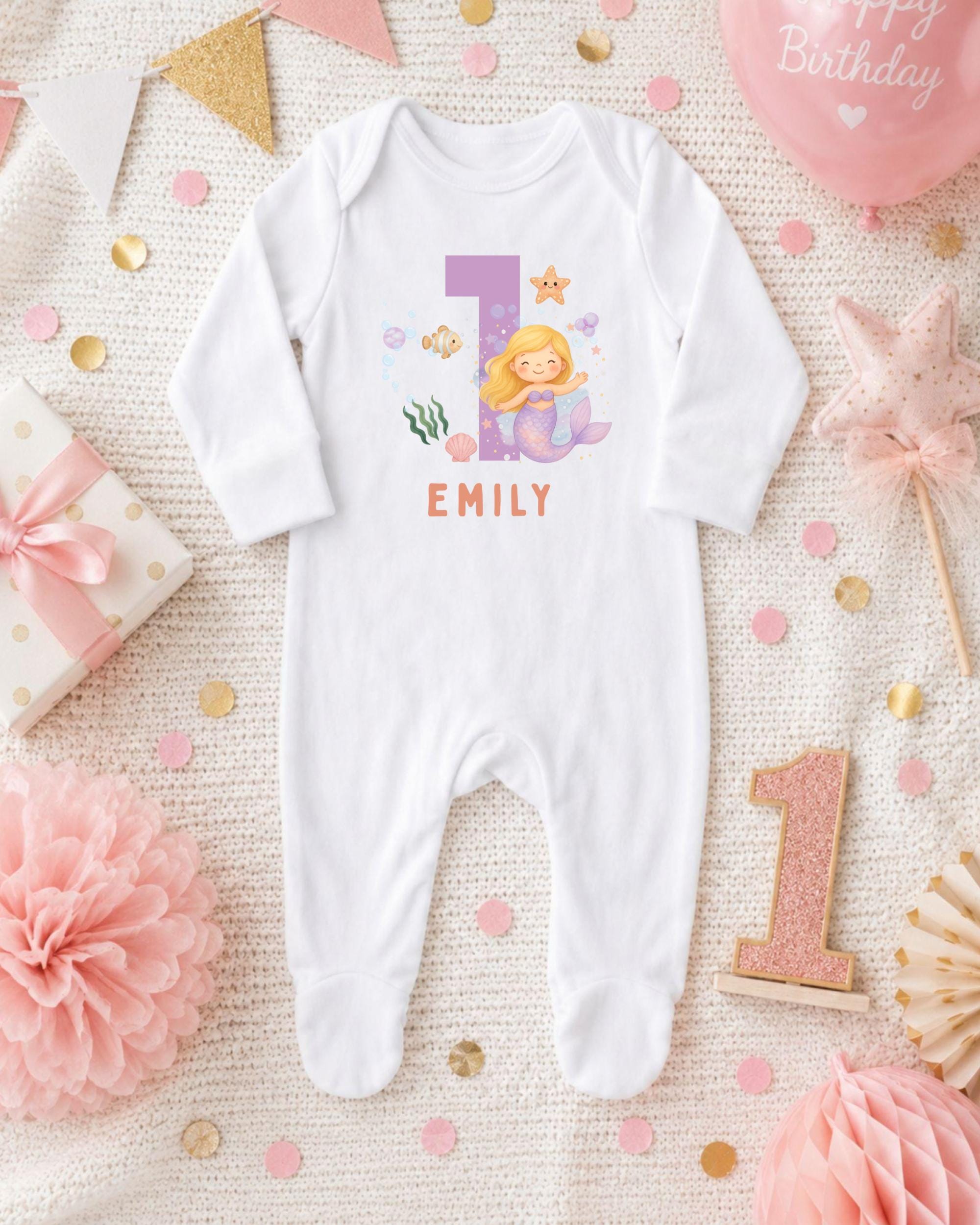 A white onesie with a mermaid design and the name "EMILY" printed on it, surrounded by pink and gold decorations, including a pink star, a pink flower, and confetti.