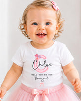 A smiling baby girl wearing a white t-shirt with a personalized monogram and a pink tutu skirt.