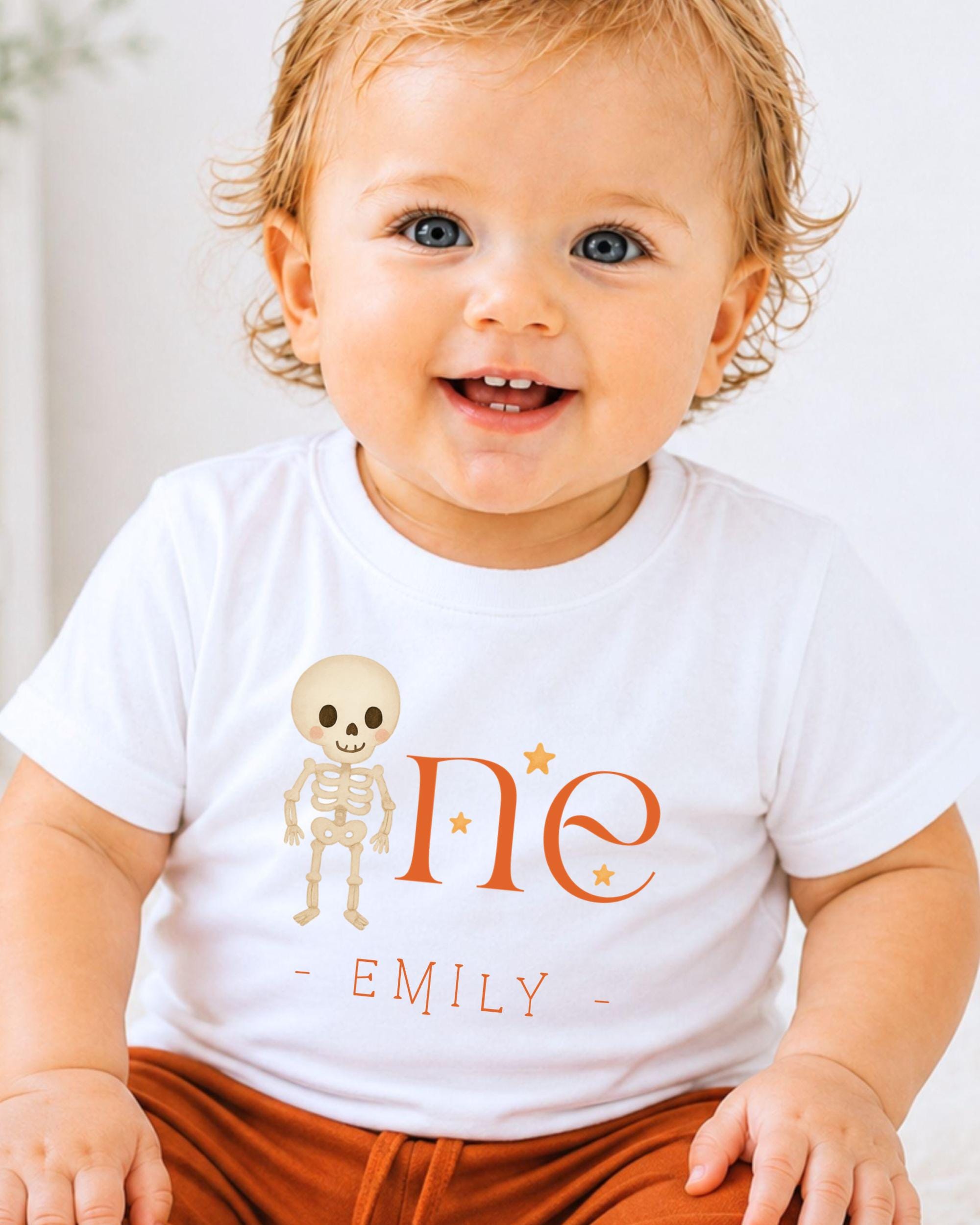 A smiling baby boy wearing a white t-shirt with a skeleton design and the name 'Emilly' printed on it.