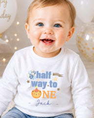 A smiling baby boy wearing a white shirt with a birthday message printed on it.