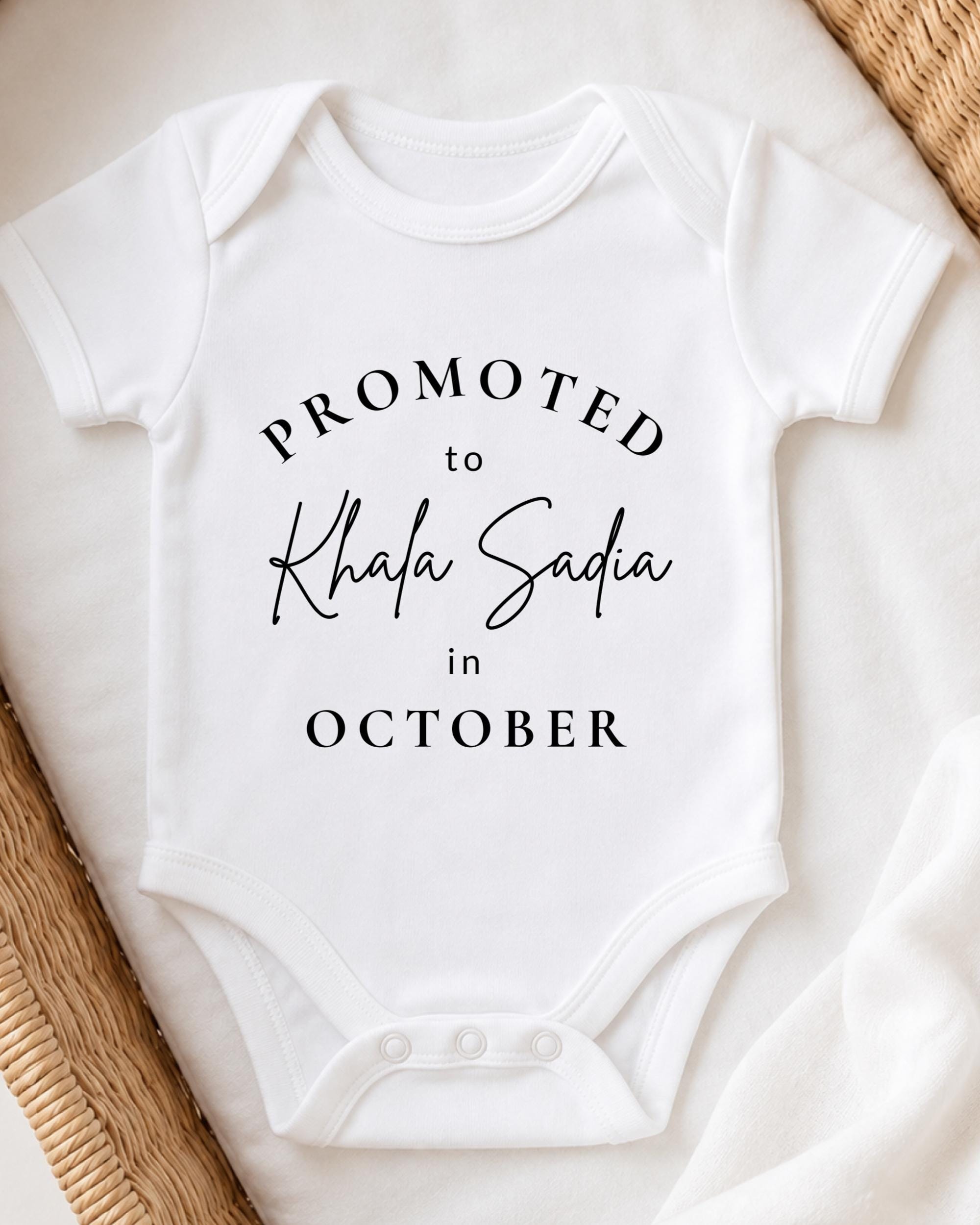 A white baby onesie with the text "PROMOTED TO Khala Sadia in October" printed on it.