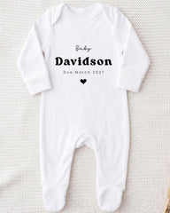 A white onesie with the text "Baby Davidson Due March 2027" printed on it.