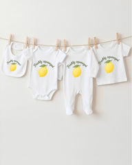 A collection of baby clothes, including onesies and bibs, hanging on a clothesline with a lemon graphic printed on them.
