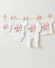 A collection of baby clothes, including onesies and bibs, hanging on a clothesline.