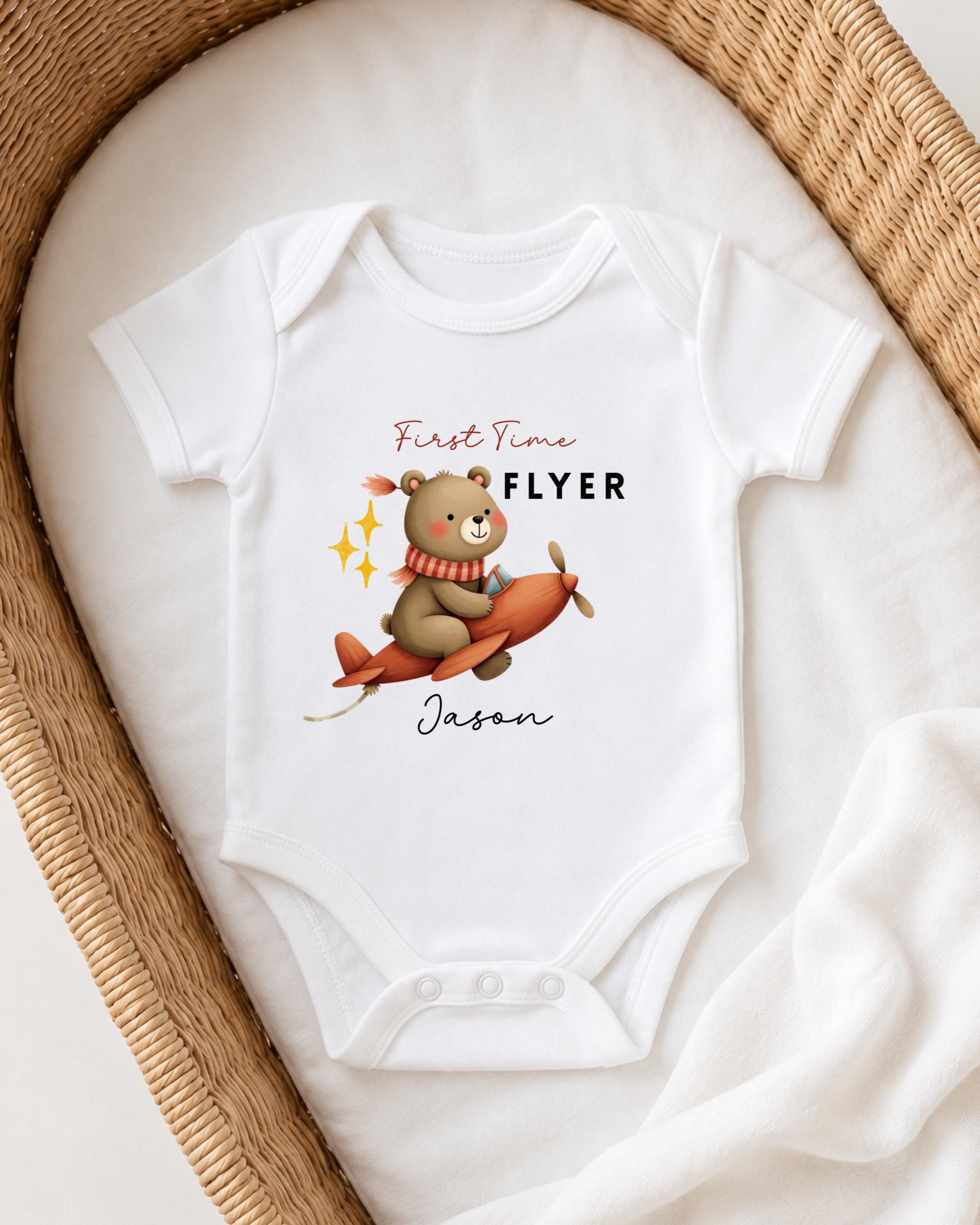 A white onesie with a cartoon image of a bear on an airplane, along with the text "First Time Flyer Jason" printed on it.