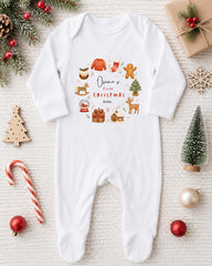 A white onesie with a Christmas-themed design, surrounded by various Christmas decorations and ornaments, including a small Christmas tree, a snow globe, and a candy cane.