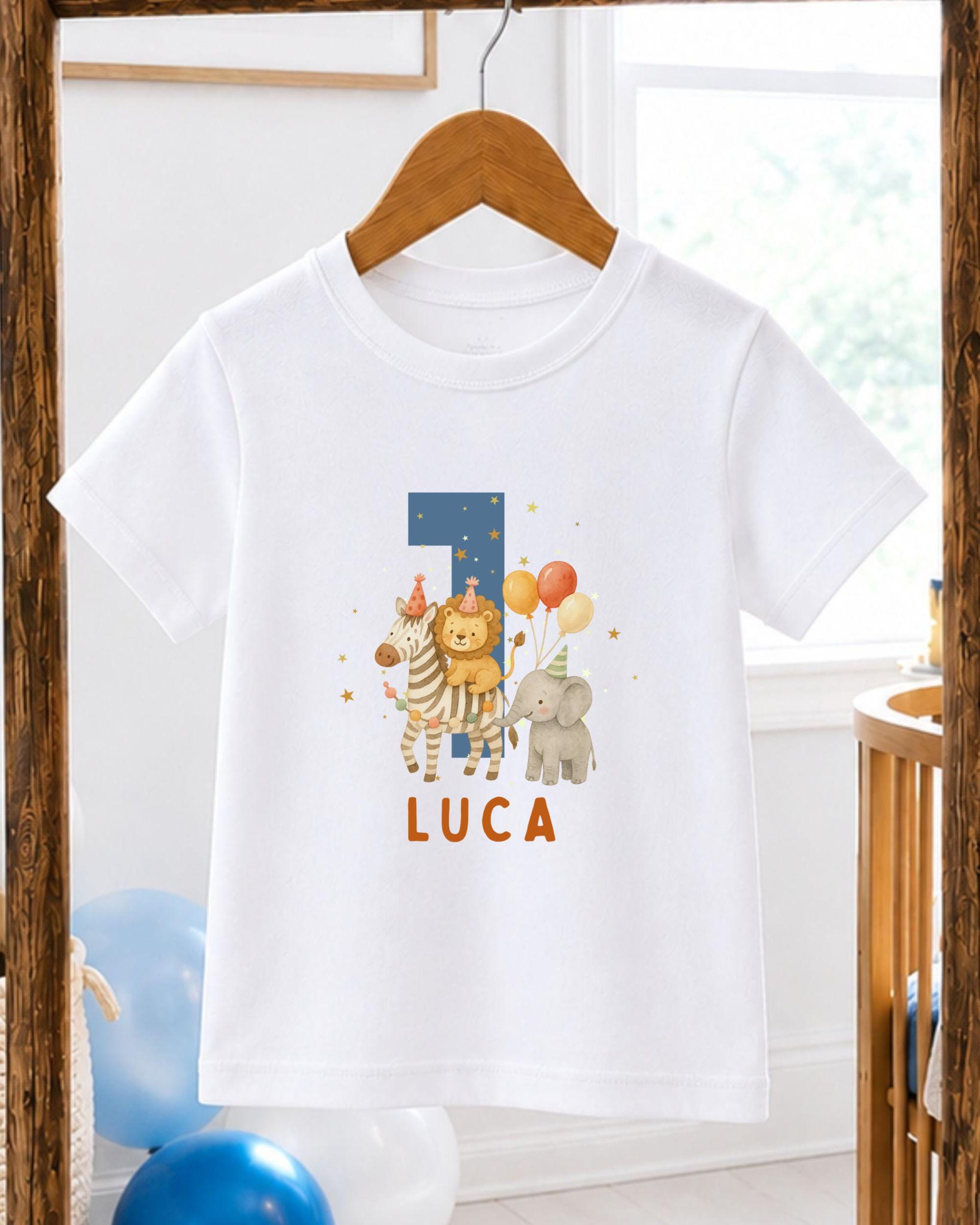 A white t-shirt with a personalized print of a lion, zebra, and elephant, along with the name 'LUCIA' printed on it, hanging on a wooden hanger.