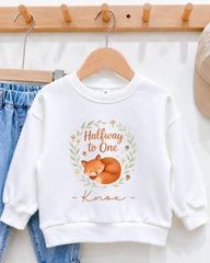 A white sweatshirt with a graphic of a sleeping fox and the text "Halfway to One" printed on it, hanging on a wooden hanger.