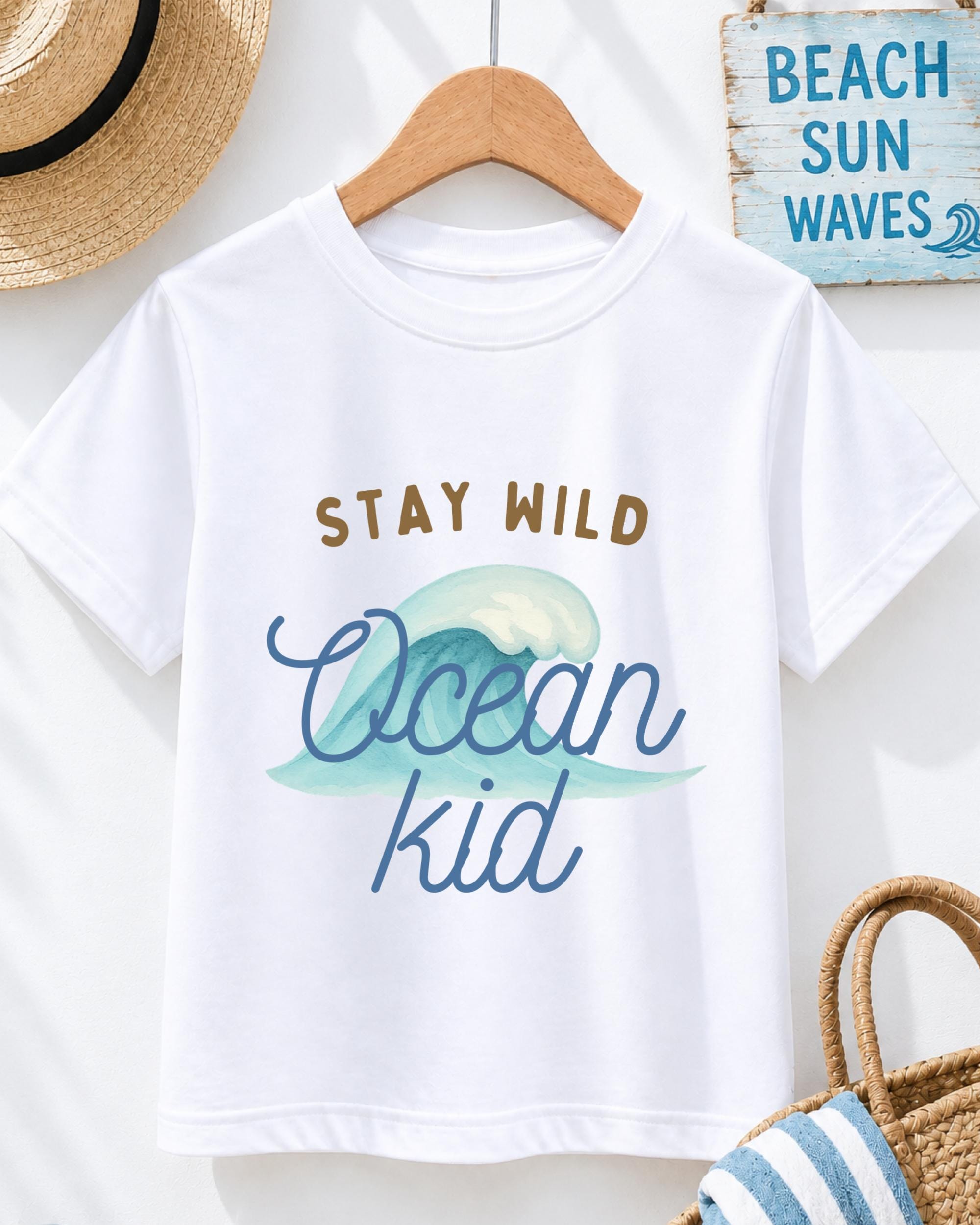 A white t-shirt with a graphic design of a wave and the text "STAY WILD Ocean kid" printed on it, hanging on a wooden hanger.