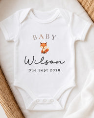 A white baby onesie with the text "BABY Wilson Due Sept 2028" printed on it, along with a small illustration of a fox.
